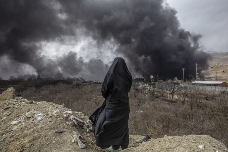 Một người phụ nữ quan s&aacute;t những cột kh&oacute;i bốc l&ecirc;n từ một kho chứa dầu v&agrave;o ng&agrave;y 8 th&aacute;ng 3 sau c&aacute;c cuộc đ&igrave;nh c&ocirc;ng đ&ecirc;m trước đ&oacute; ở Tehran. Ảnh của Arash Khamooshi. Từ cnn.com